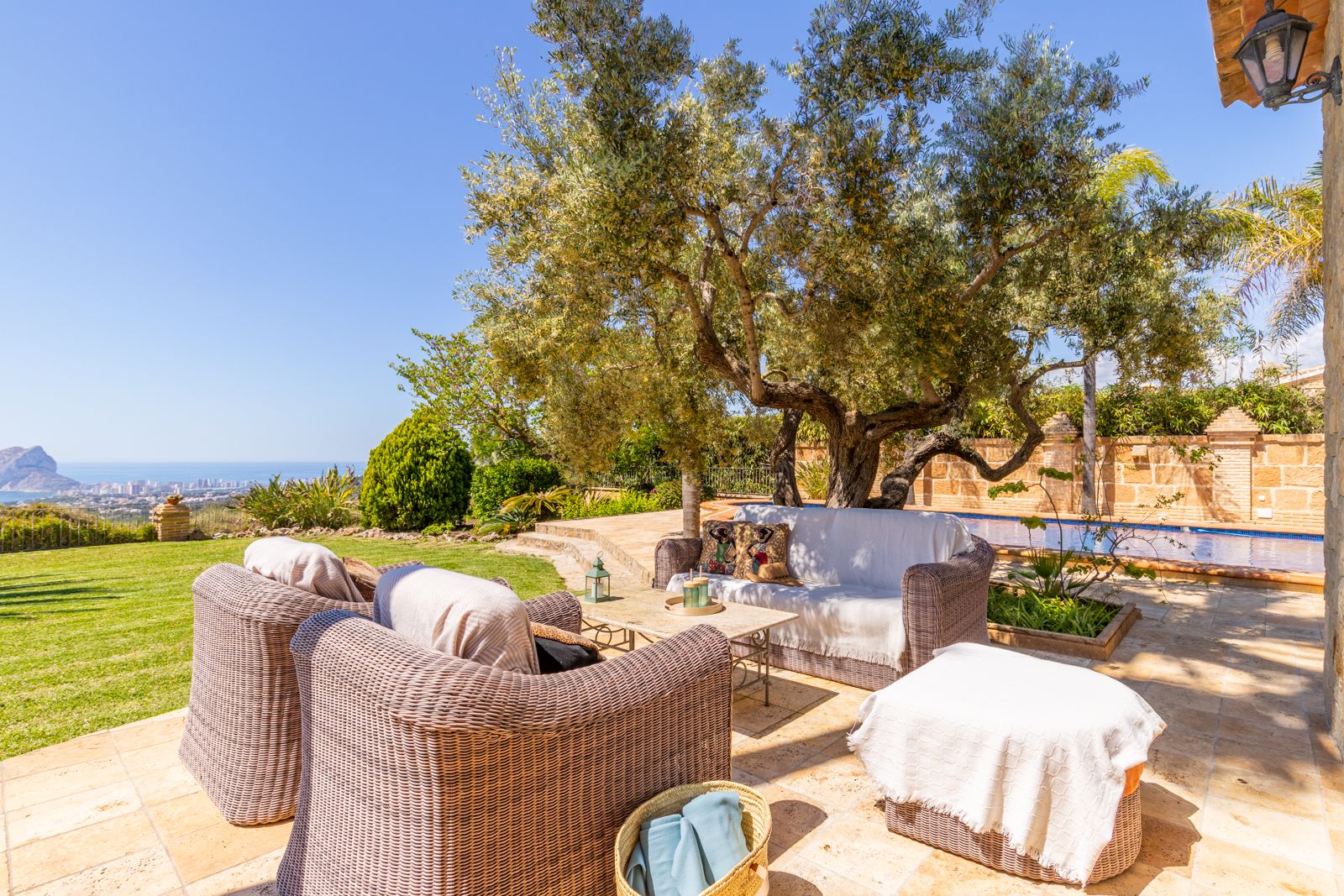 Terrace featuring wicker furniture with sea views, shaded by a mature olive tree.