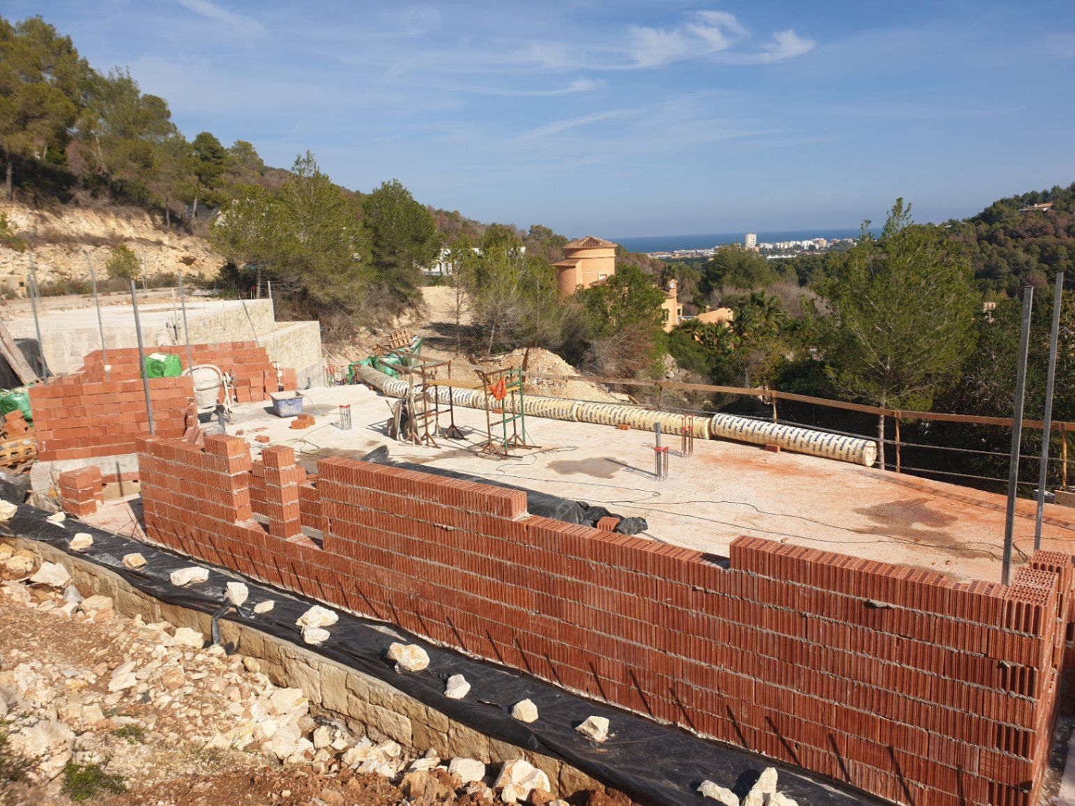 Current construction phase featuring ceramic brick walls on the foundation slab, overlooking the Mediterranean Sea and the pine-covered hills of Jávea.