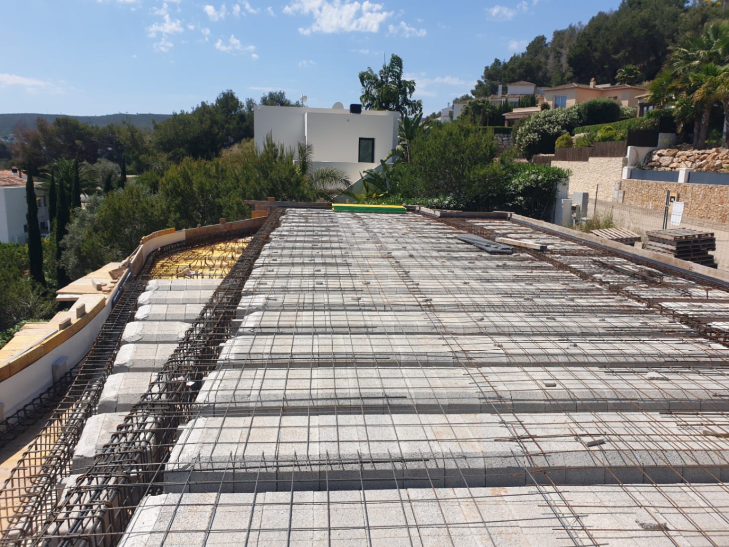 Current construction phase showing the floor slab assembly with concrete blocks and steel reinforcement mesh overlooking the Jávea landscape.