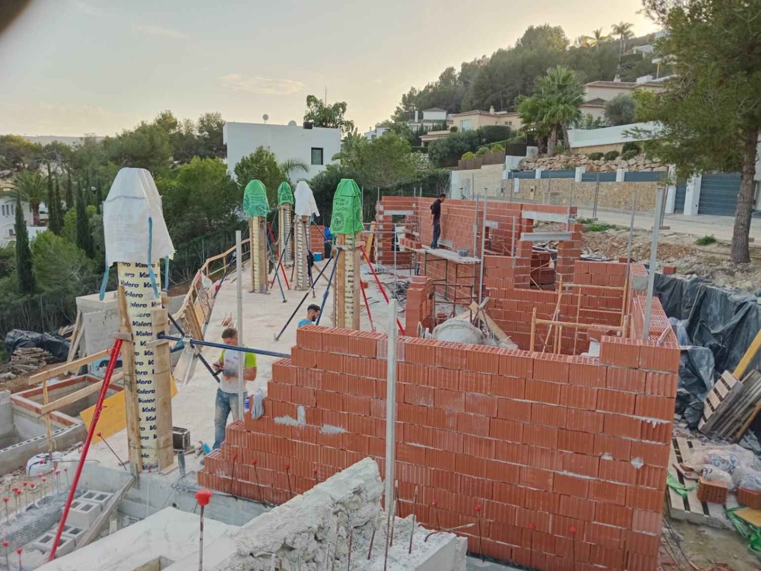 Current construction progress featuring ceramic brick walls and structural columns on an elevated plot overlooking the surrounding Mediterranean landscape.