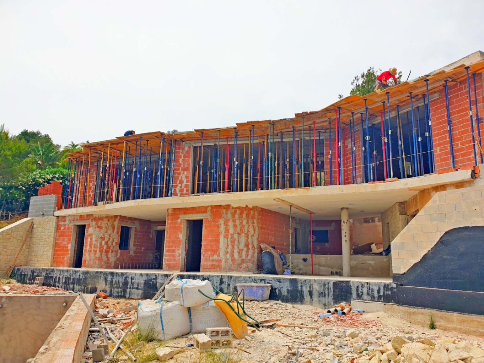 Exterior view of the villa during the construction phase, highlighting the brick structure, concrete slabs, and the elegant curved lines of the upper level.