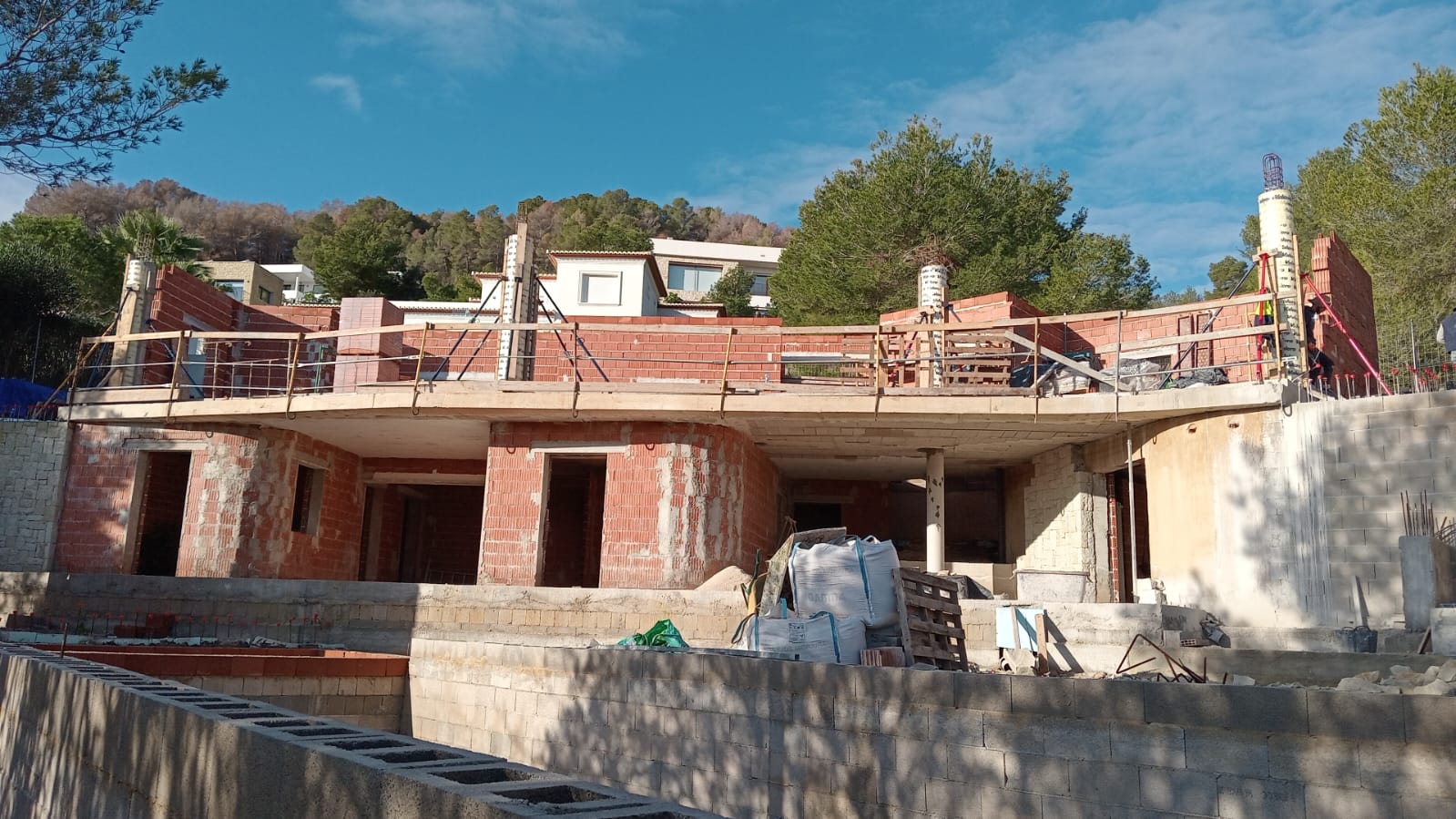 Exterior view of the villa under construction, highlighting the curved concrete terrace and the brick structure of the two living levels.