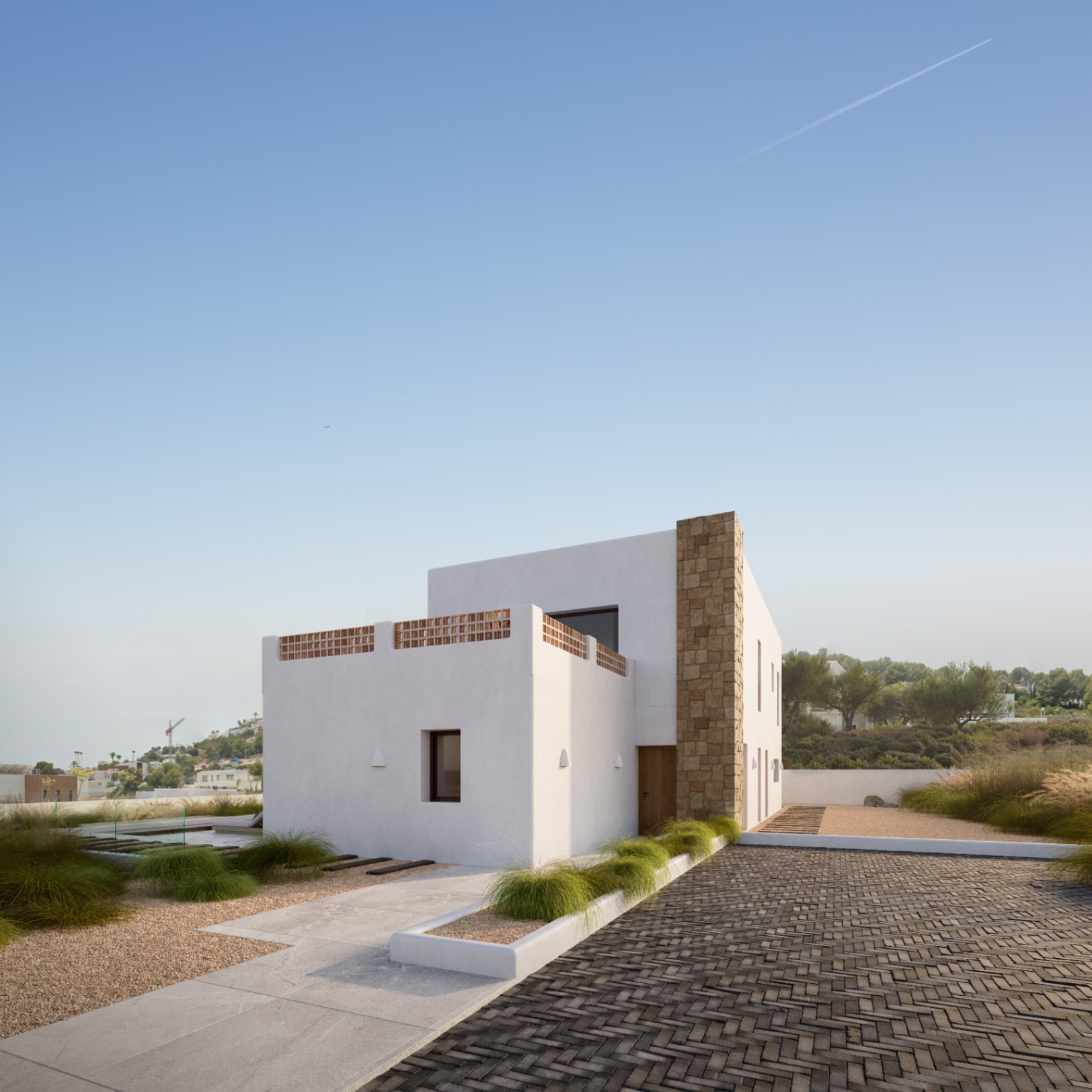 Modern Mediterranean facade featuring white walls, a natural stone pillar, and a terrace with terracotta lattice work, set within minimalist landscaping and paved paths.