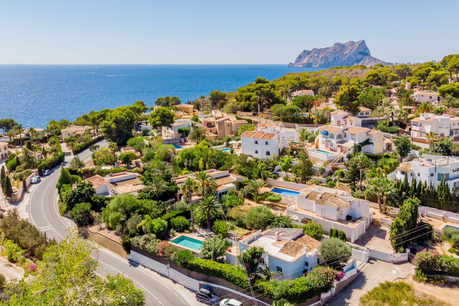 Aerial view of the Baladrar coastline featuring the Peñón de Ifach. This residential area offers proximity to the Mediterranean Sea amidst lush pine and palm trees.