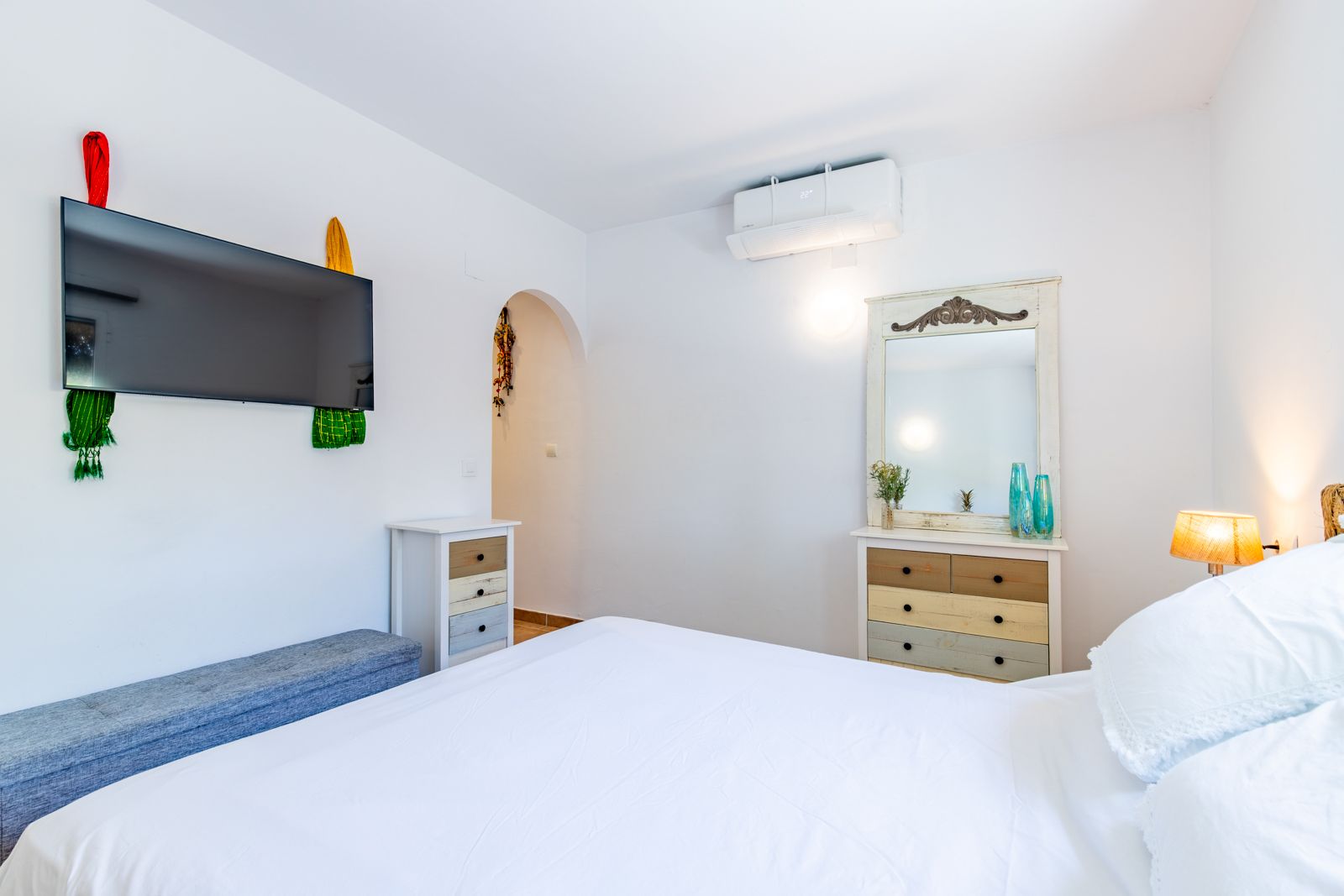 Bright bedroom featuring a double bed, rustic-style wooden dressers, wall-mounted TV, and split air conditioning for year-round comfort.