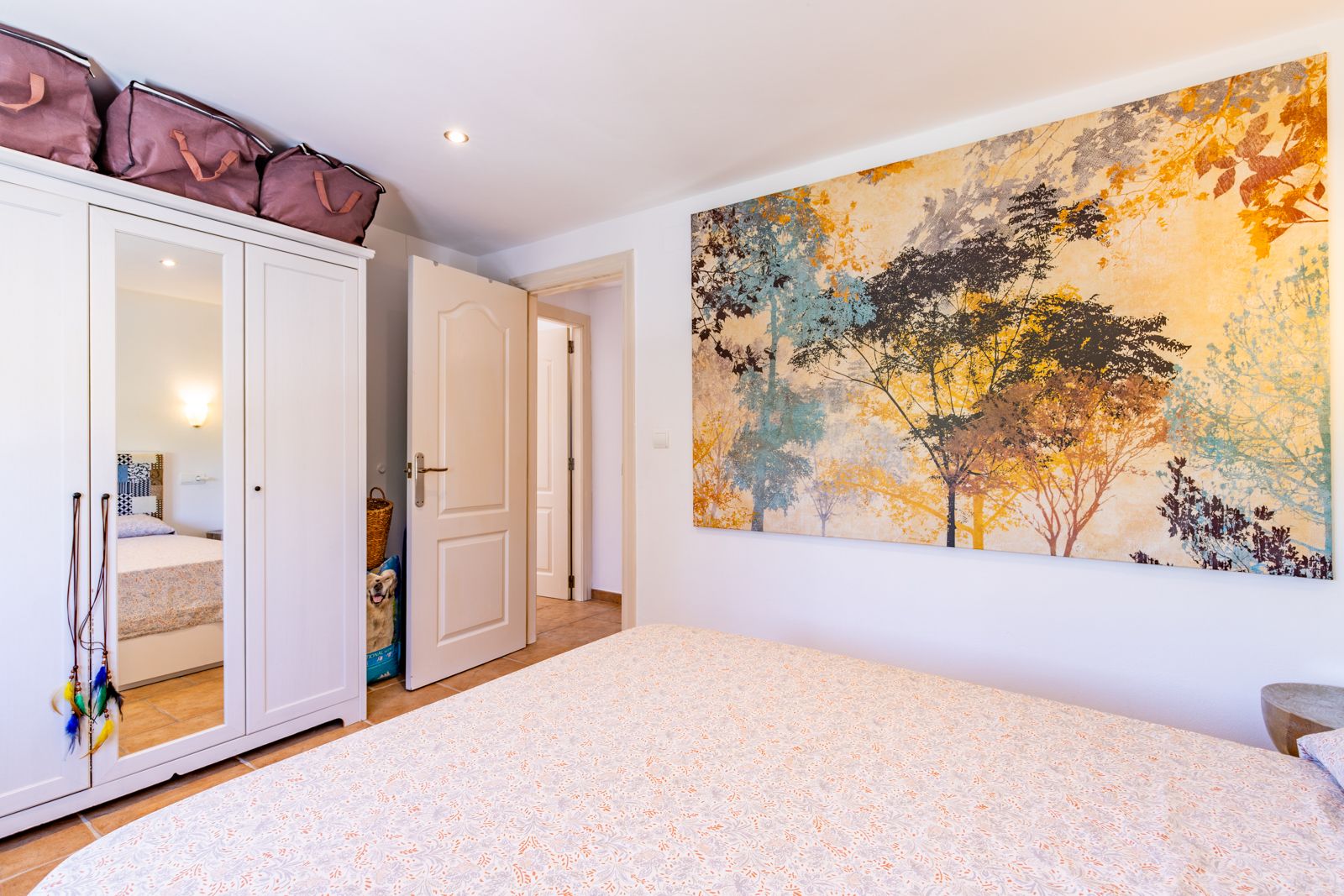 Bright bedroom featuring a white three-door wardrobe with a central mirror and a large nature-themed wall mural. Tiled flooring and recessed ceiling lighting.