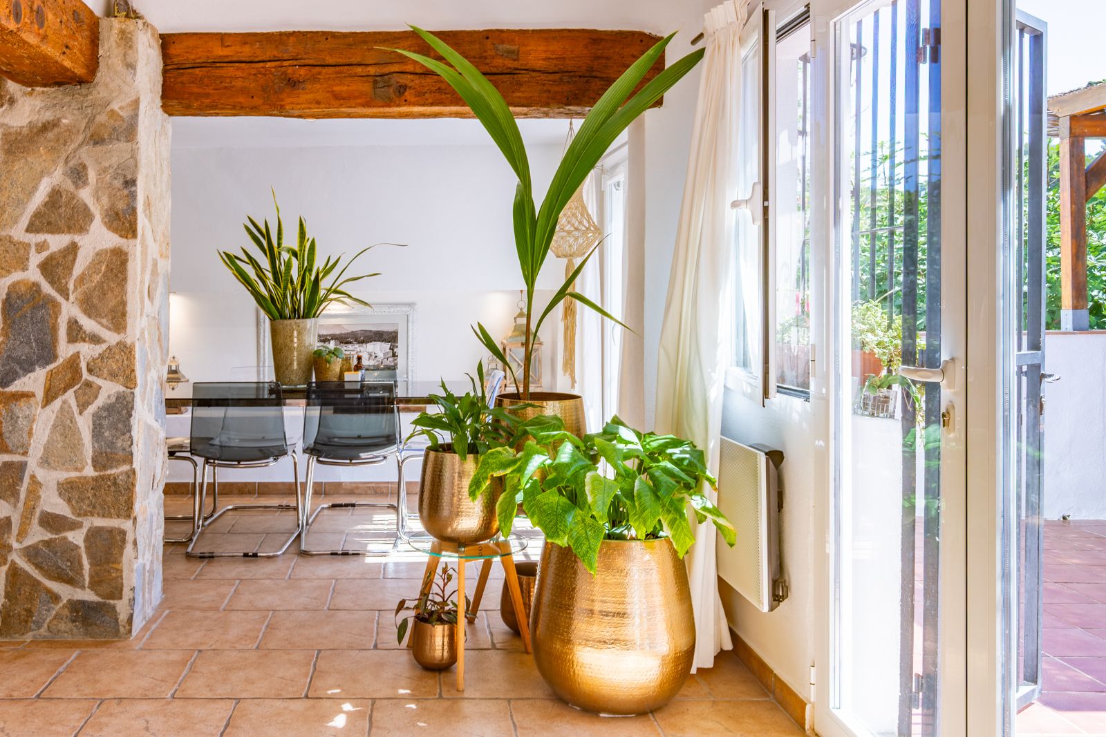 Interior living space featuring exposed rustic wooden beams, a natural stone pillar, and terracotta flooring. Large glass doors provide direct access to the terrace.