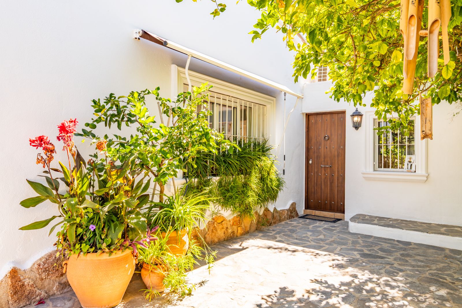 Main entrance featuring a rustic wooden door, natural stone paving, and terracotta planters against a traditional white facade.