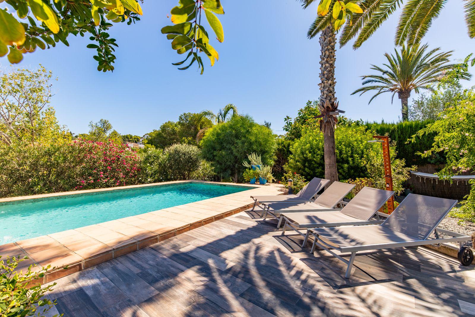 Private swimming pool with terracotta coping and a tiled sun deck featuring four modern loungers, set within a lush Mediterranean garden.
