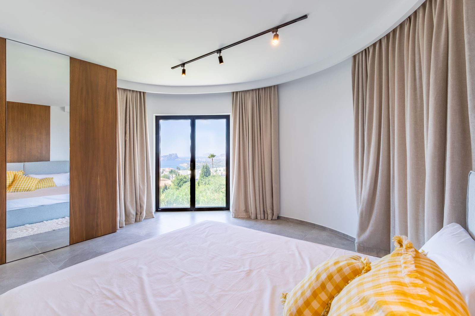 Bedroom featuring a curved wall, custom oak cabinetry with mirrored door, and panoramic coastal views through high-efficiency sliding glass doors.