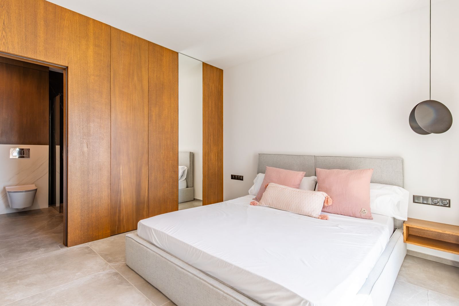 Bedroom featuring custom floor-to-ceiling oak paneling, large-format porcelain tiles, and an en-suite bathroom with high-end stone finishes.