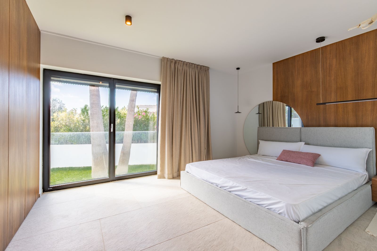 Bedroom featuring natural oak wall paneling, large-format porcelain flooring, and direct garden access through high-efficiency sliding glass doors.