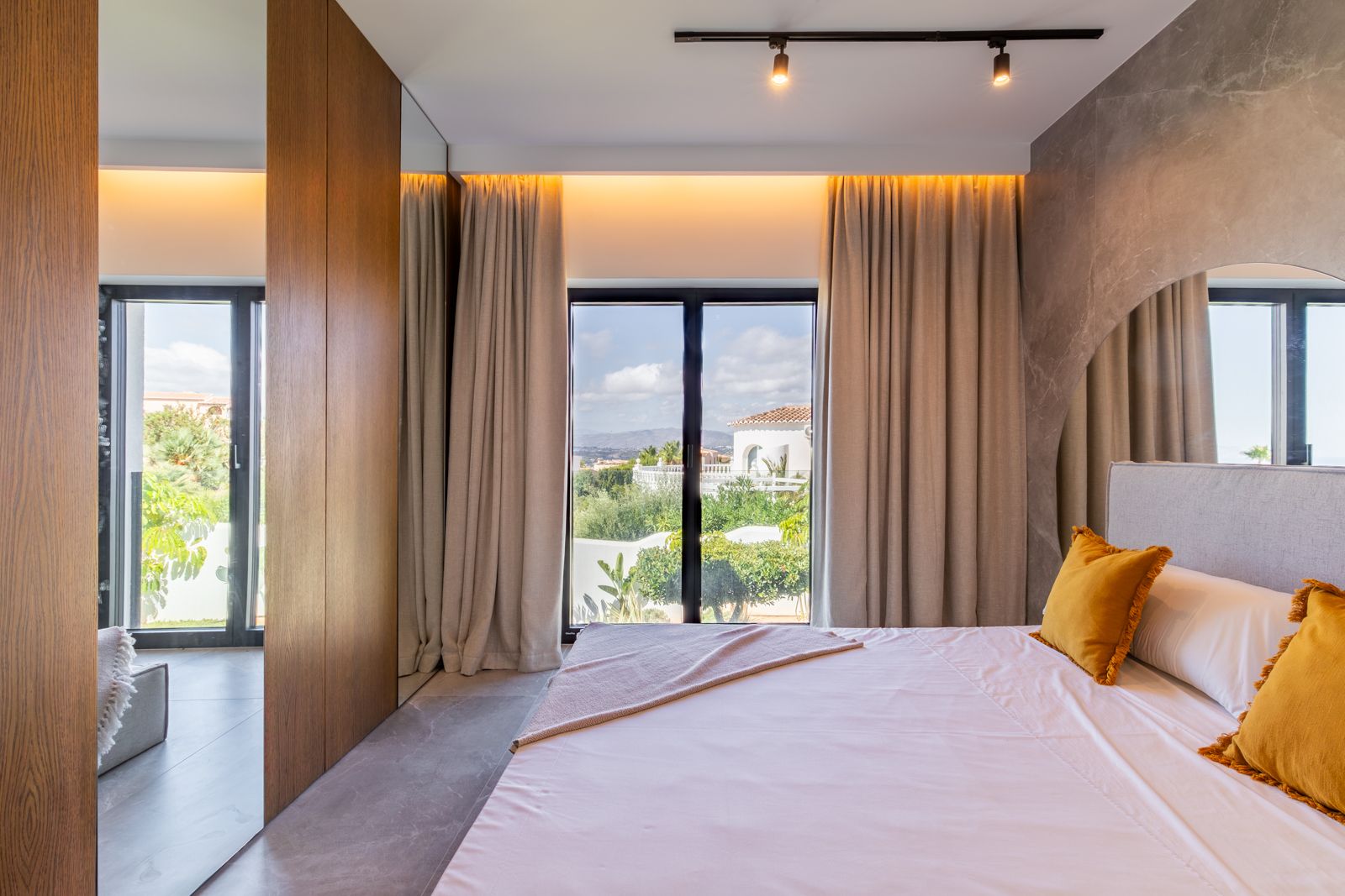 Bedroom featuring natural oak wall paneling, porcelain flooring, and large windows offering views of the Mediterranean garden and landscape.