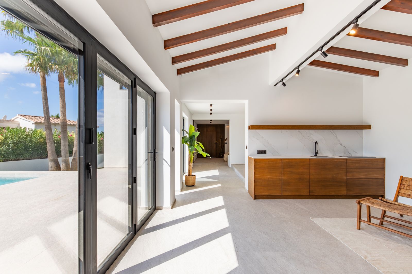 Bright open-plan space featuring exposed wooden beams, a custom oak kitchenette, and large sliding glass doors that integrate the interior with the pool area.