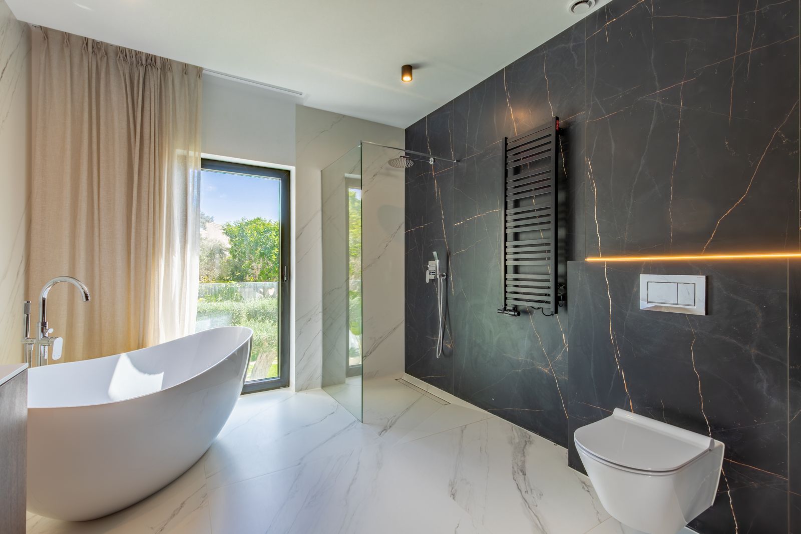 Designer bathroom featuring a freestanding bathtub, walk-in shower, and contrasting porcelain wall panels. Includes a wall-hung toilet, black towel rail, and garden views.