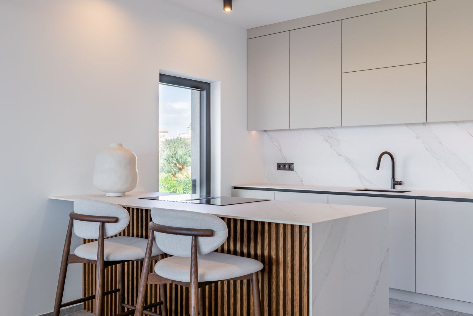 Designer kitchen featuring a marble-effect sintered stone island with vertical wood slats, integrated induction hob, and minimalist black fixtures against neutral cabinetry.
