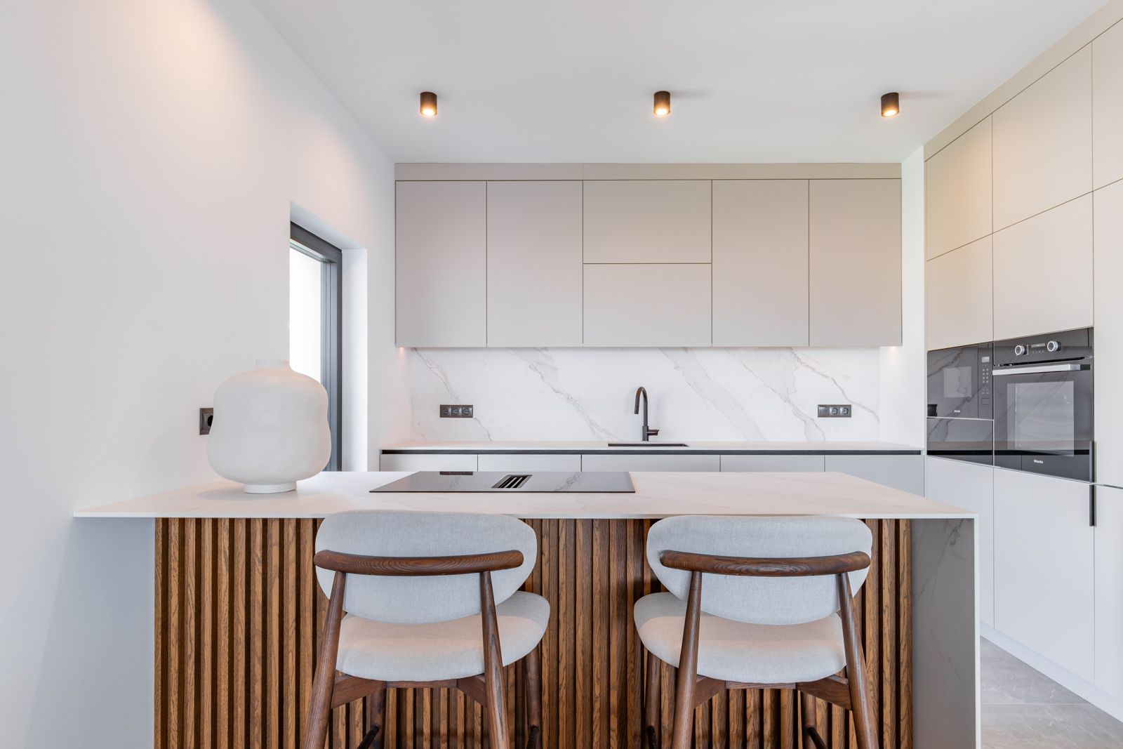 Designer kitchen featuring an oak-slatted island, sintered stone countertops, and integrated Miele appliances within minimalist, handleless cabinetry.