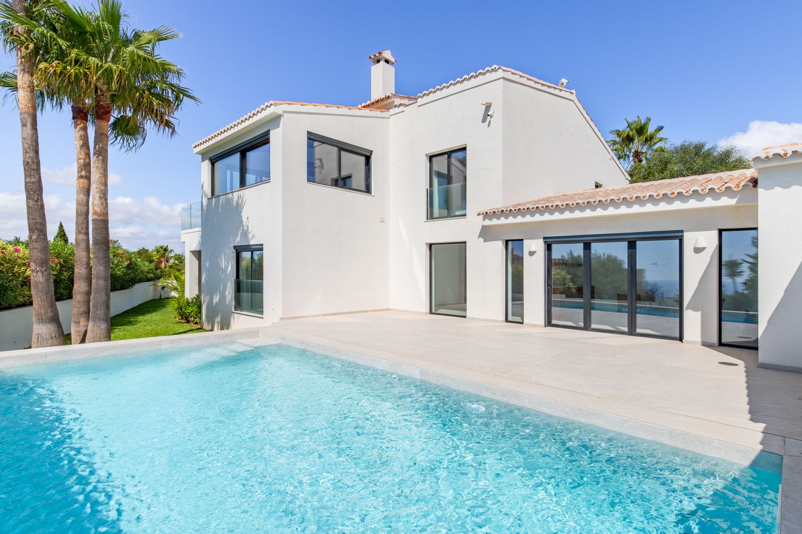 Exterior view featuring a salt-chlorinated pool and a large porcelain tile terrace. The white facade integrates high-performance aluminum windows and triple-glazed glass.