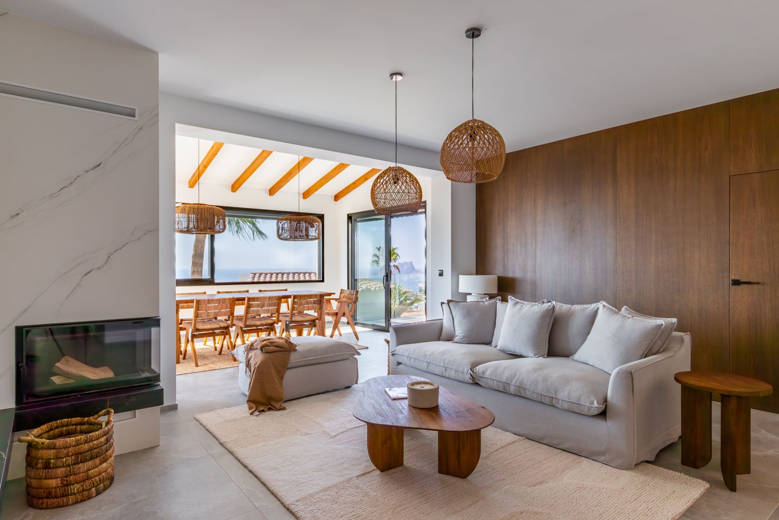Living room featuring a built-in fireplace, natural oak wall paneling, and Mediterranean views. Includes woven pendant lights and a dining area with exposed beams.