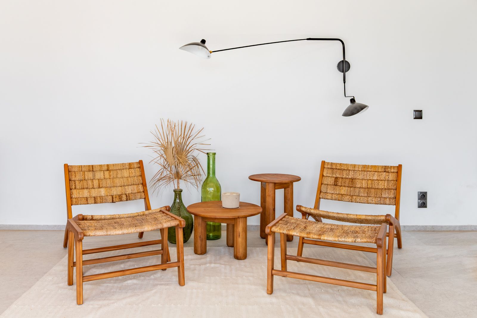 Lounge area featuring wooden chairs with woven fiber seats, teak side tables, and a black designer swing-arm lamp against a neutral porcelain floor.