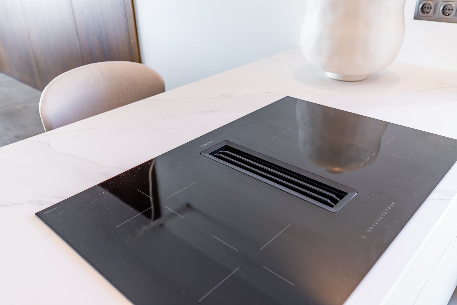 Miele induction cooktop with integrated downdraft extractor set into a white marble-effect sintered stone countertop.
