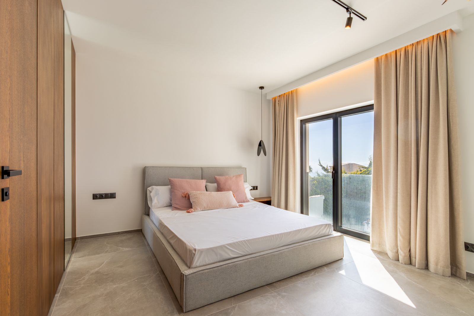 Modern bedroom featuring large-format porcelain flooring, custom oak cabinetry with integrated mirror, and direct terrace access through high-efficiency glazing.
