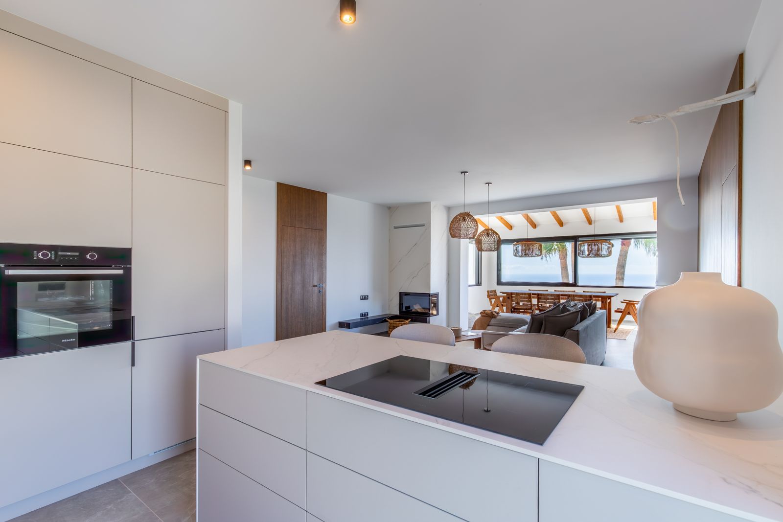 Open-plan designer kitchen featuring a sintered stone island with integrated induction, Miele appliances, and views extending to the living area and Mediterranean Sea.