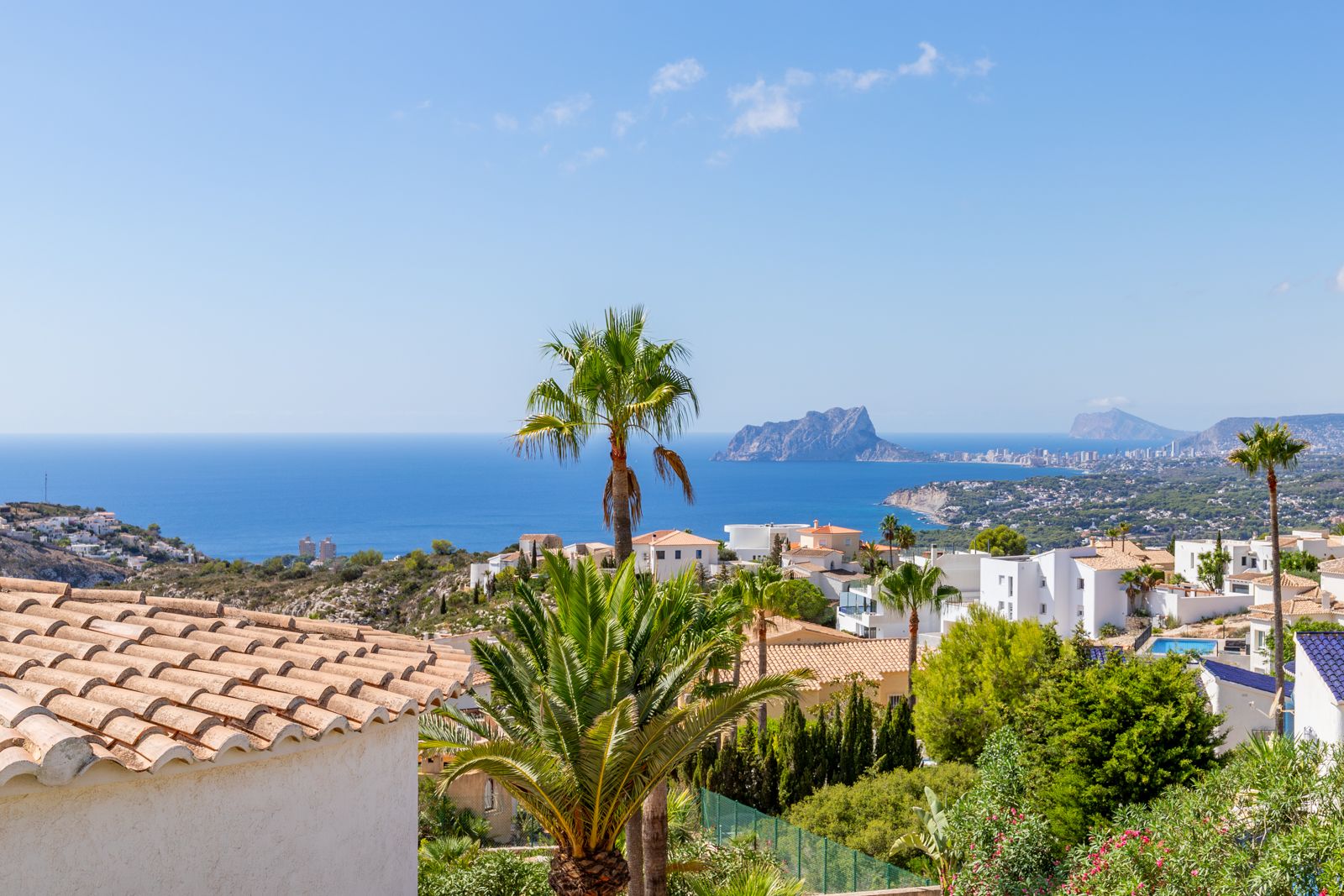 Panoramic views of the Mediterranean Sea and the Peñón de Ifach, featuring coastal architecture and lush palm trees under a clear sky.