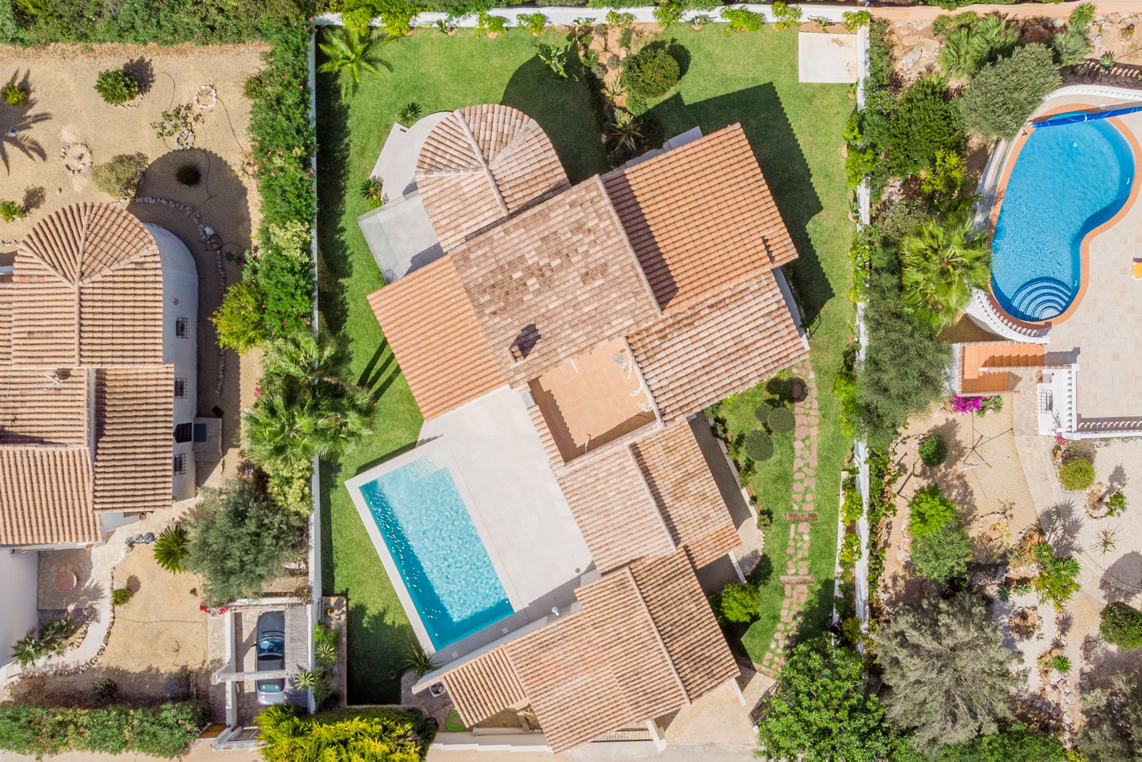 Top-down aerial view showing the villa's terracotta tiled roof, the rectangular swimming pool, and the manicured lawn with perimeter landscaping.