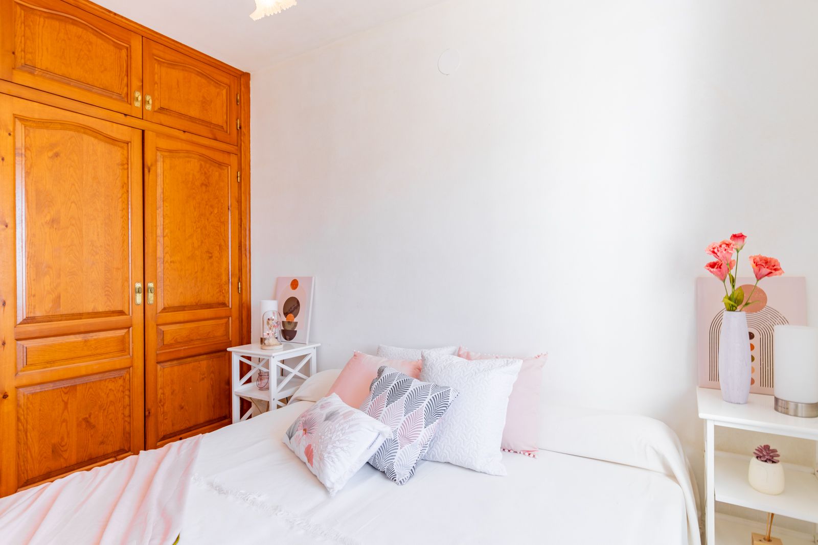 Bright bedroom featuring a large built-in wooden wardrobe with traditional paneling, white walls, and minimalist side tables for a clean, functional space.