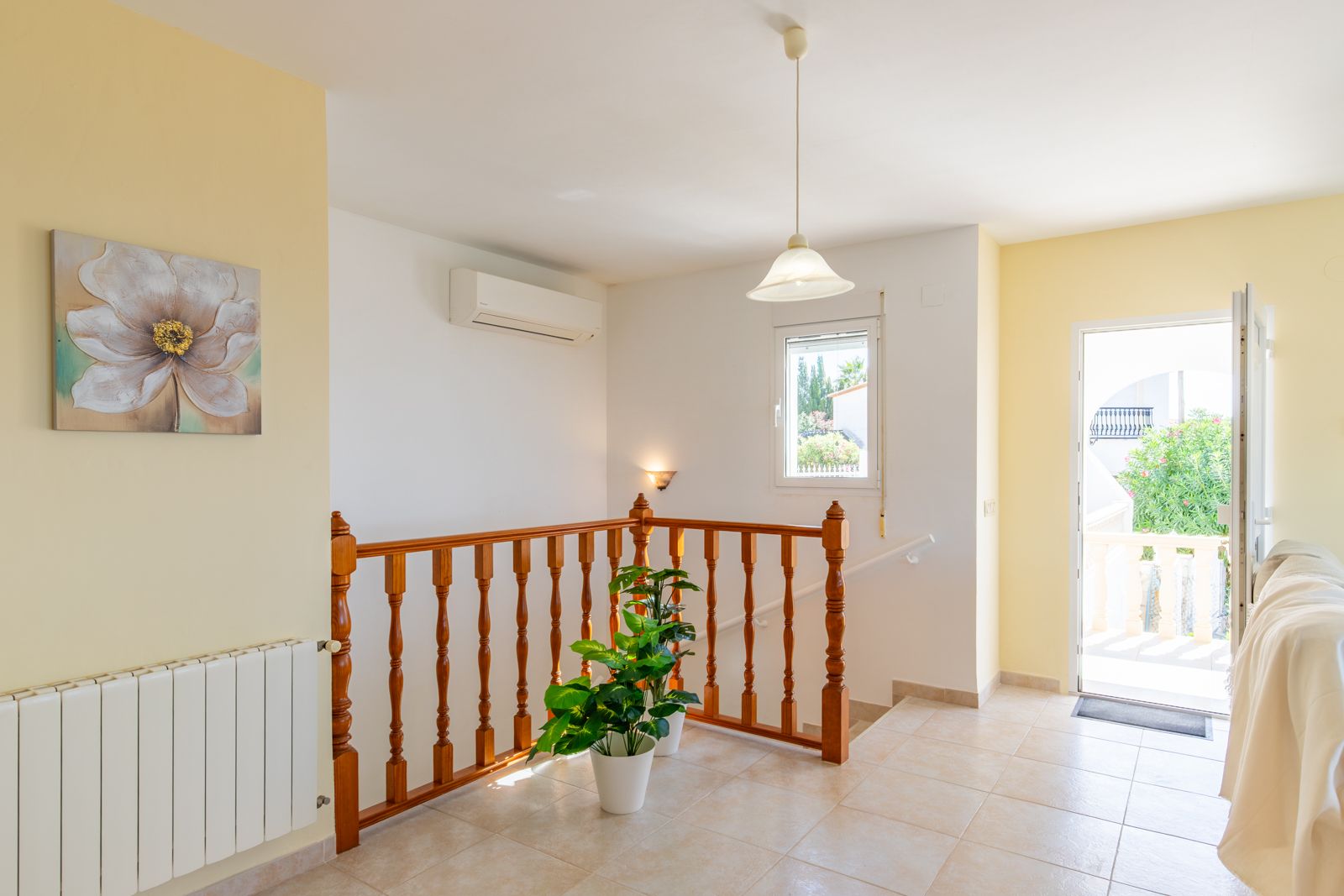 Bright landing featuring ceramic tile flooring, a traditional wooden balustrade, and terrace access. Equipped with a wall-mounted air conditioning unit and central heating.