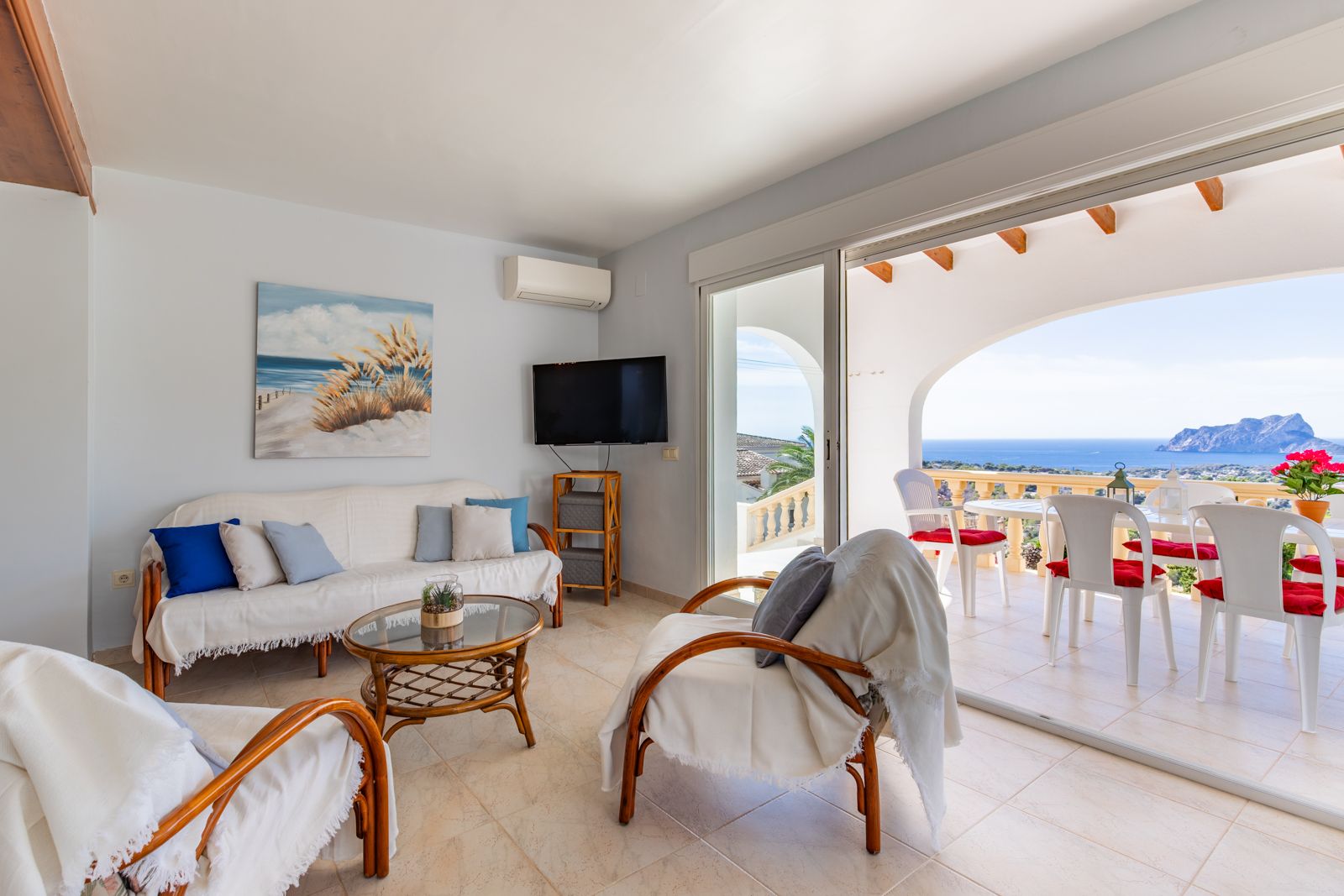 Bright living area featuring rattan furniture and sliding doors that open to a covered terrace. It offers panoramic views of the Mediterranean Sea and Peñón de Ifach.