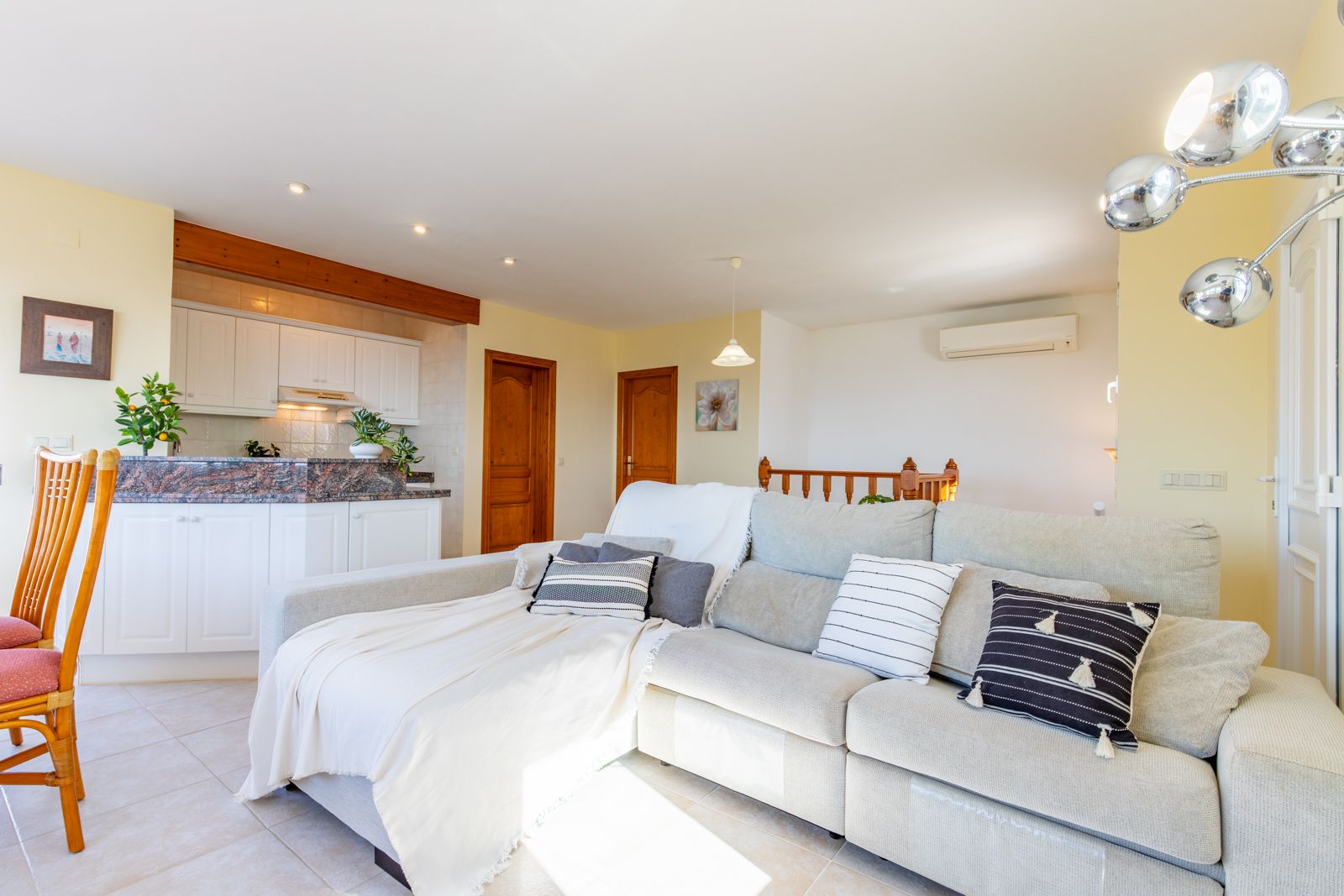 Bright living space featuring a large L-shaped sofa, open-plan kitchen with granite countertops, wooden beams, and split-system air conditioning.