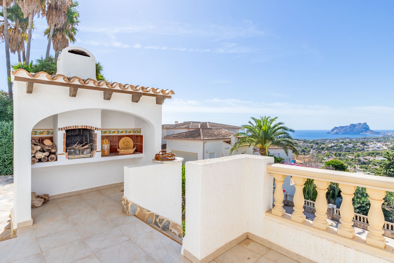 Built-in masonry barbecue with a chimney and decorative tiling on an elevated terrace, featuring panoramic views of the Mediterranean and Peñón de Ifach.