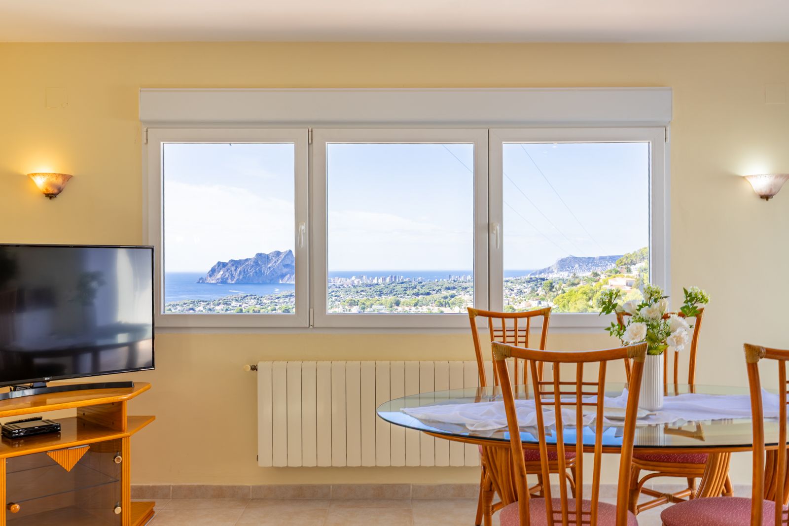 Dining area featuring a large window with panoramic views of the Mediterranean Sea and Peñón de Ifach. Equipped with central heating and a glass-top table.