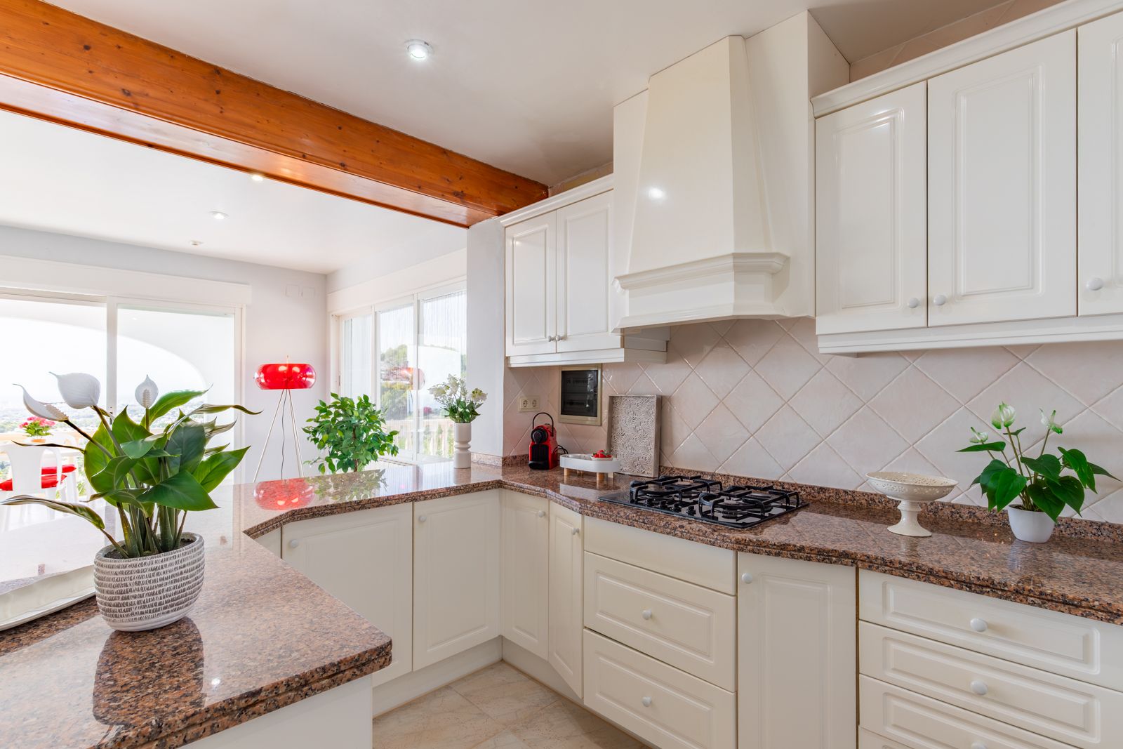 Equipped kitchen featuring granite countertops, classic white cabinetry, and exposed wooden beams, opening into a bright living and dining area.