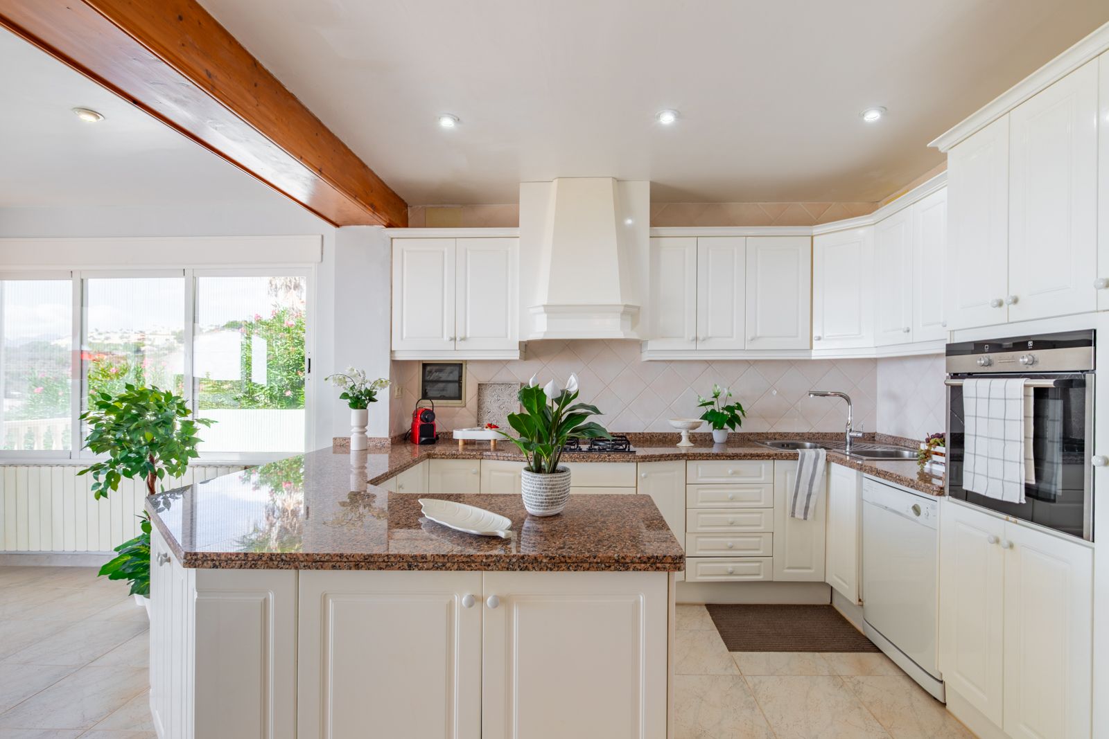 Fully equipped kitchen featuring white cabinetry, granite countertops, and integrated appliances. It includes a wooden ceiling beam, recessed lighting, and a breakfast bar.