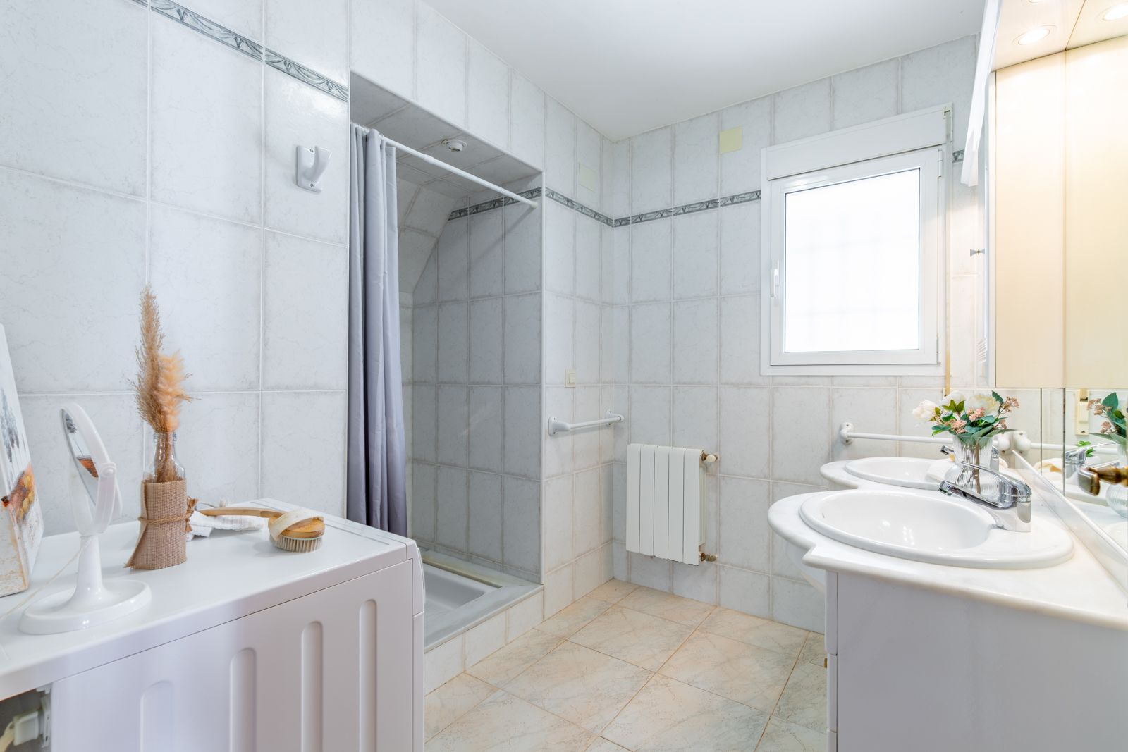 Functional bathroom featuring a double marble vanity, integrated laundry space, walk-in shower, and central heating radiator with natural light.