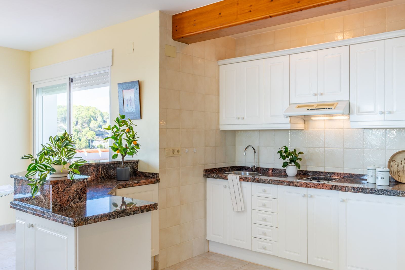 Functional kitchen featuring dark granite countertops, classic white cabinetry, and an exposed wooden beam. Large windows provide natural light and views of the surroundings.