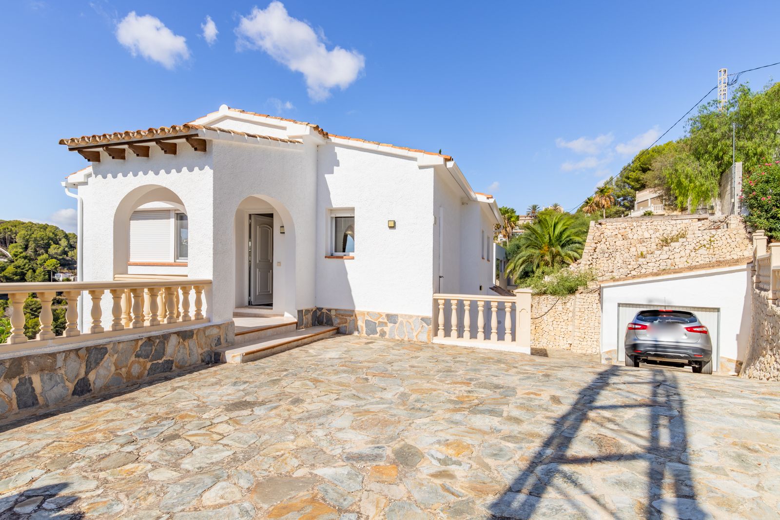 Mediterranean exterior featuring an arched entrance with wooden beams, natural stone paving, and a spacious driveway leading to the private garage.