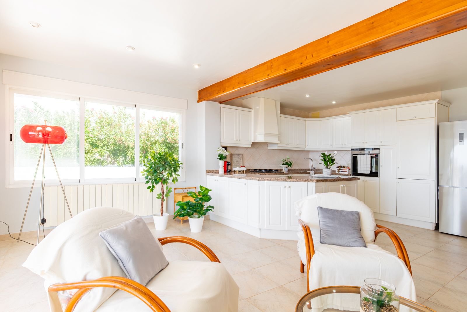 Open-plan kitchen featuring white cabinetry and granite countertops, integrated into a bright living area with exposed wooden beams and garden views.
