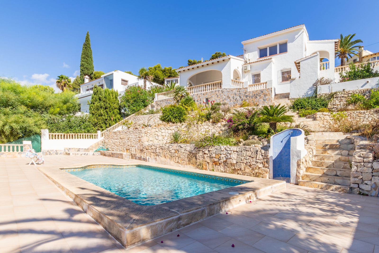 Private swimming pool featuring a stone border and sun terrace, set against terraced Mediterranean gardens with natural stone walls and an outdoor shower.