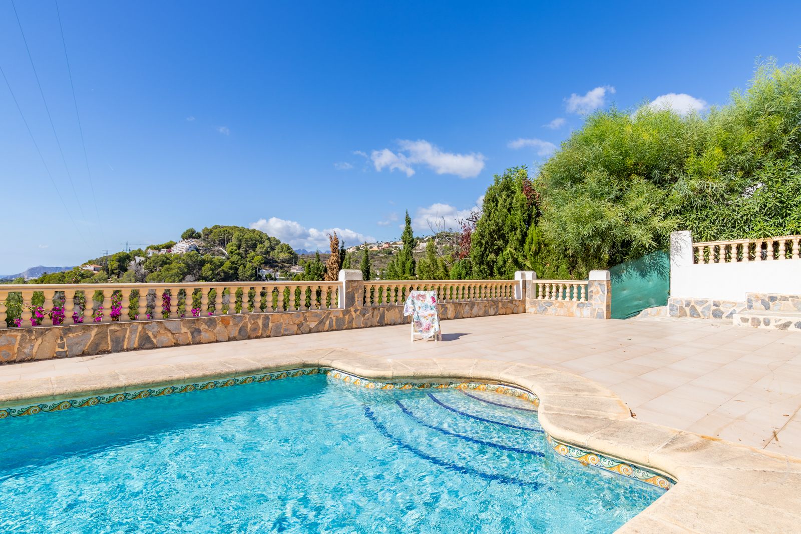 Private swimming pool featuring decorative tile borders and a spacious sun terrace, enclosed by a natural stone balustrade with clear views of the surrounding hills.