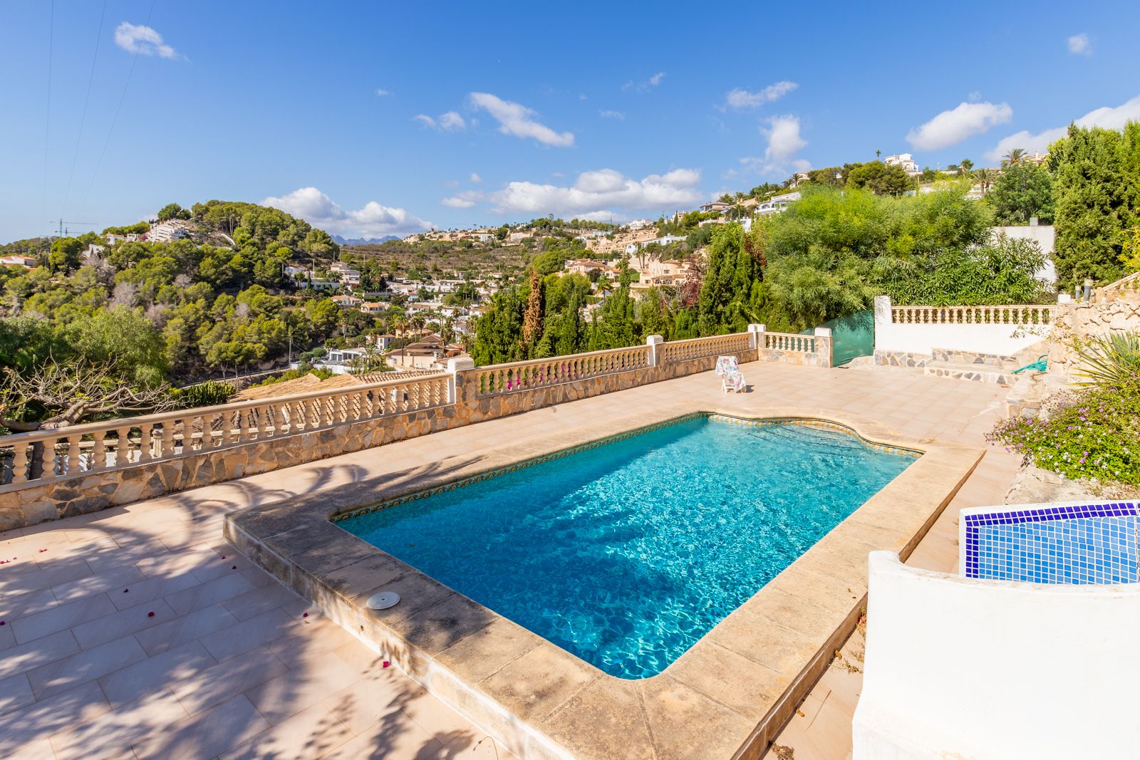 Rectangular private swimming pool set on a stone-paved terrace, featuring a classic balustrade and panoramic views of the lush Mediterranean valley.