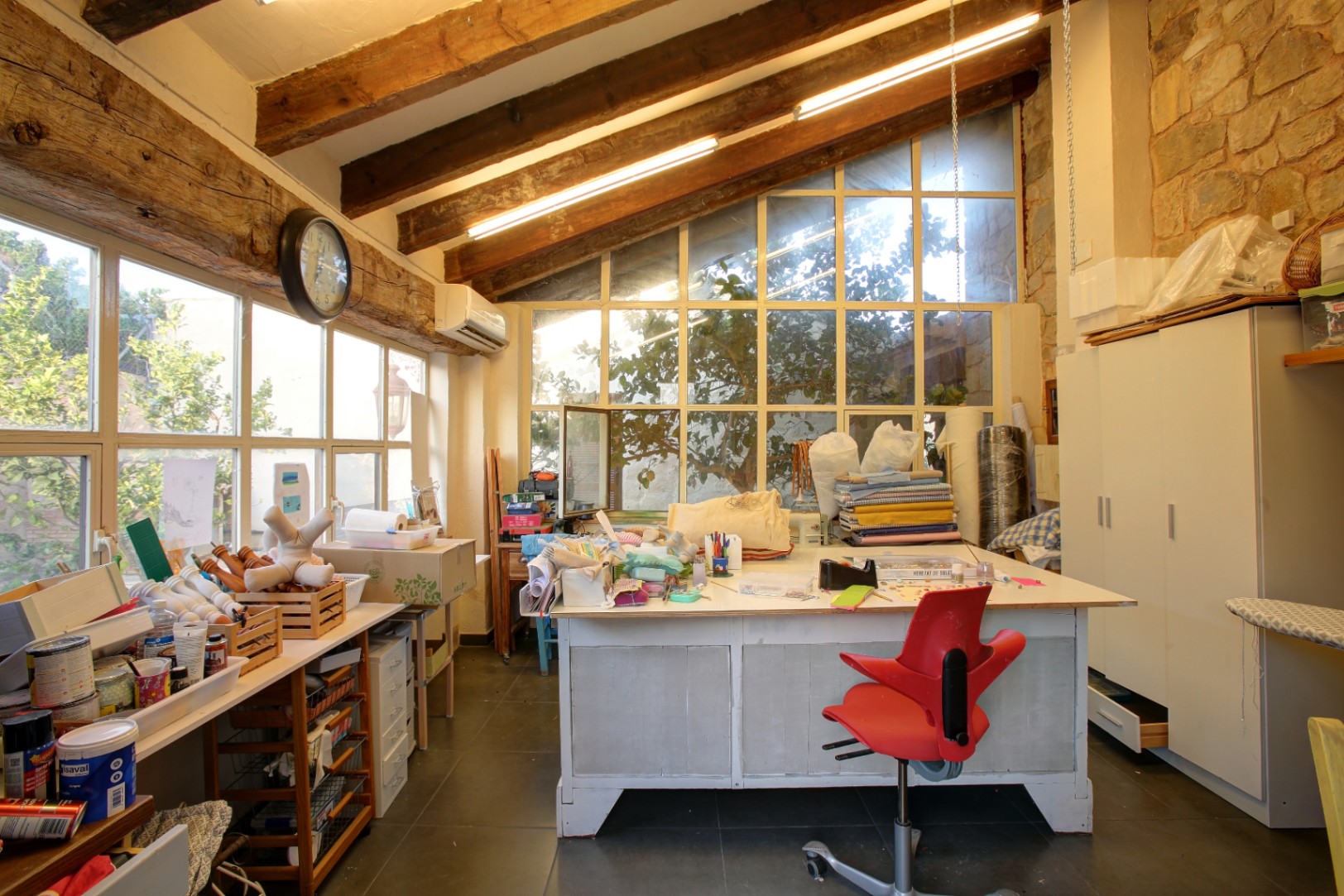Creative studio featuring reclaimed wooden beams, natural stone walls, and large windows providing abundant natural light for the workspace.