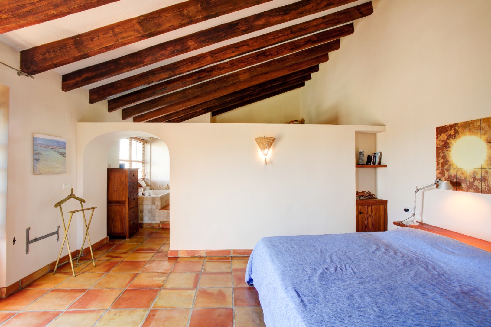 Master bedroom featuring high ceilings with exposed wooden beams, traditional terracotta tile flooring, and an arched entrance leading to the ensuite bathroom.