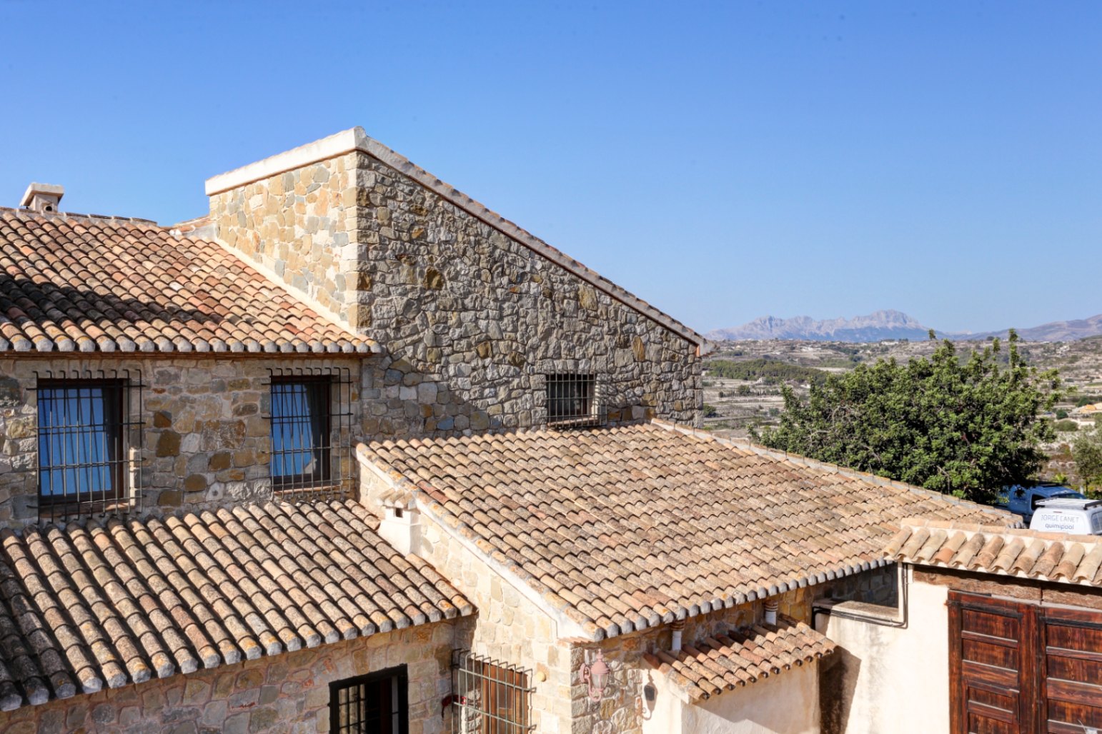 Natural stone facade and terracotta tile roofing showcasing traditional Mediterranean architecture with panoramic views of the distant mountains.