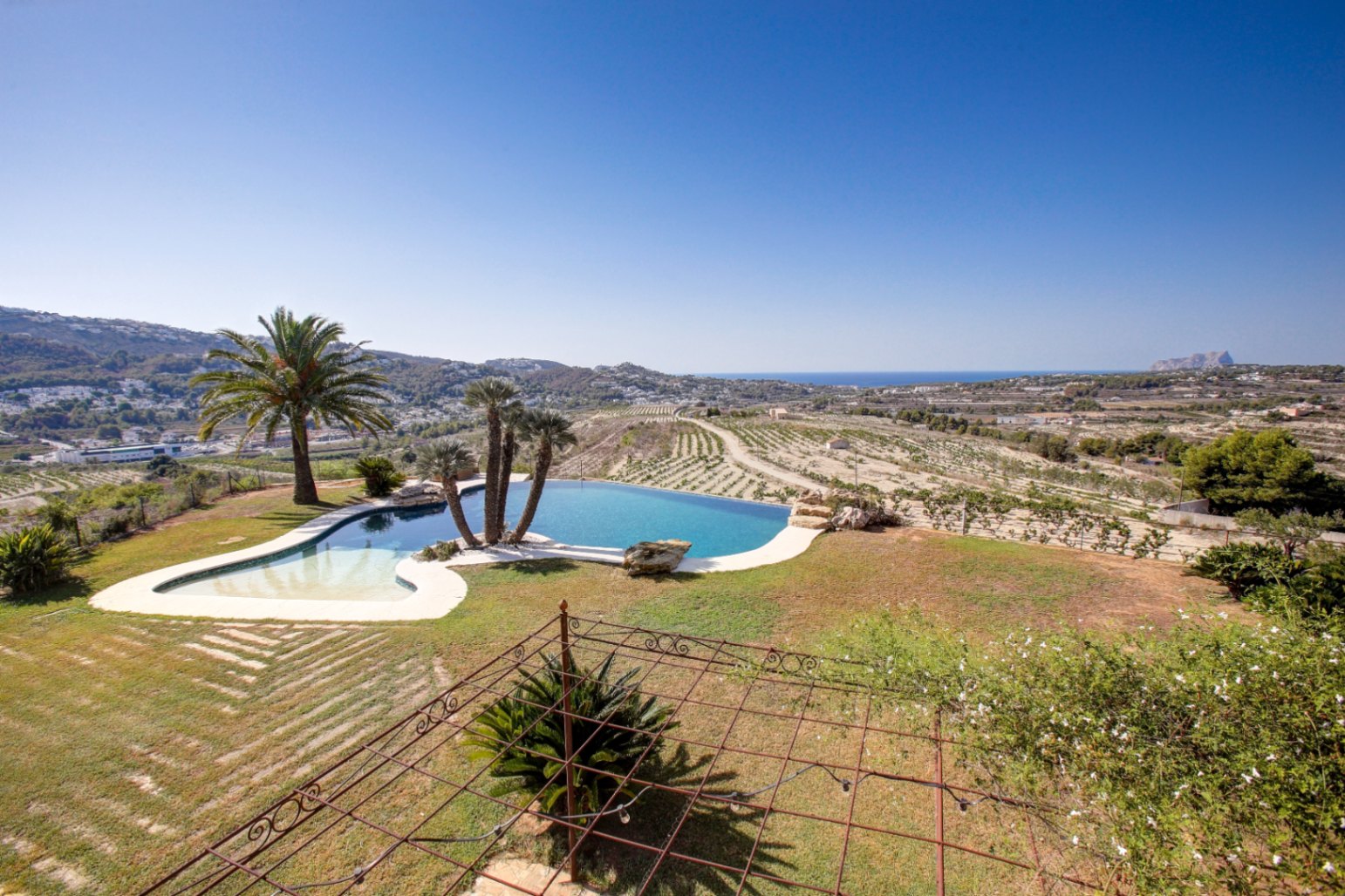 Organic-shaped infinity pool featuring panoramic Mediterranean Sea views and the Peñón de Ifach, set within a vast estate of terraced vineyards.