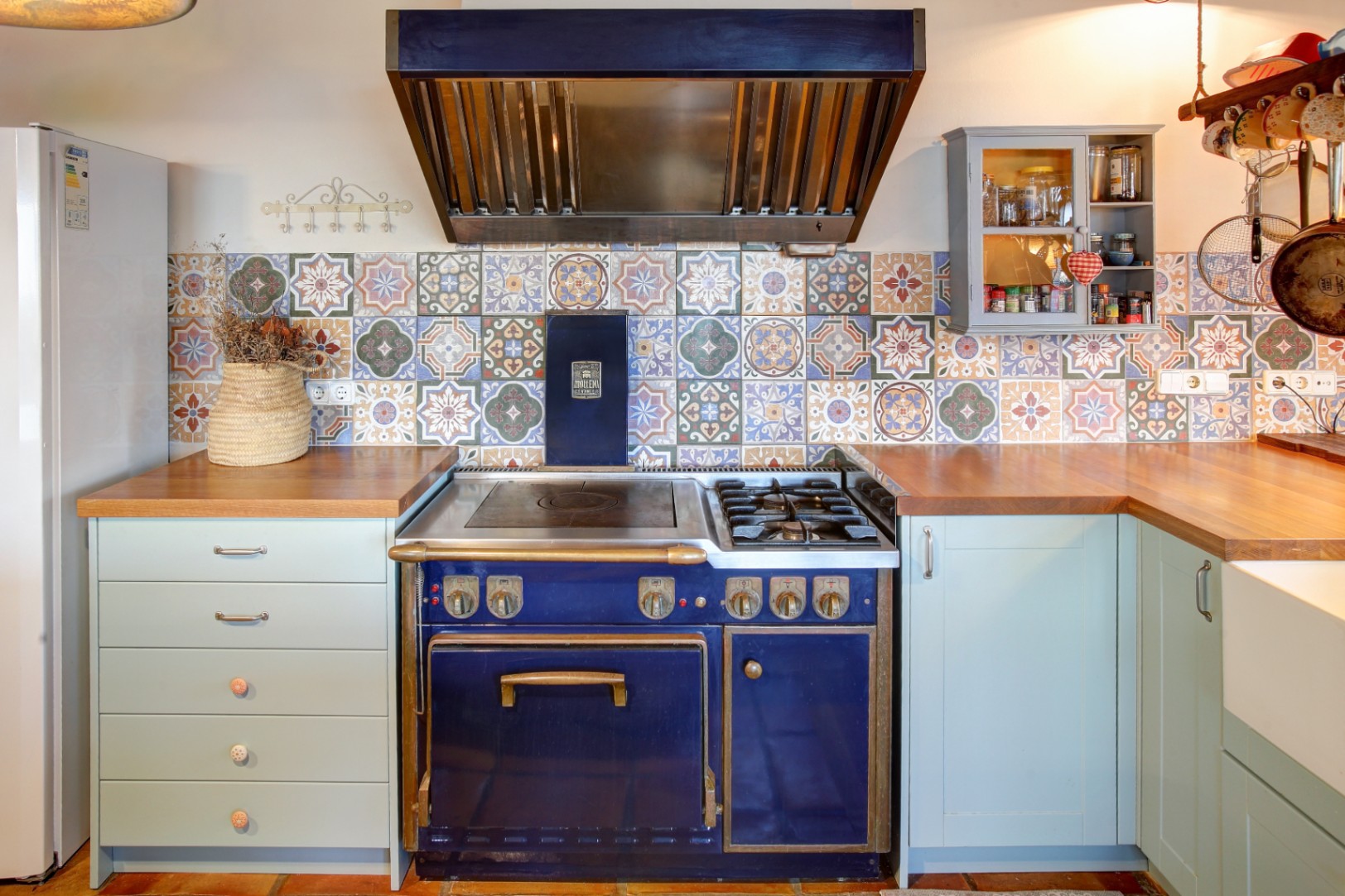 Professional blue Molteni gas range with brass accents, set against a patterned tile backsplash and solid wood countertops with light blue cabinetry.