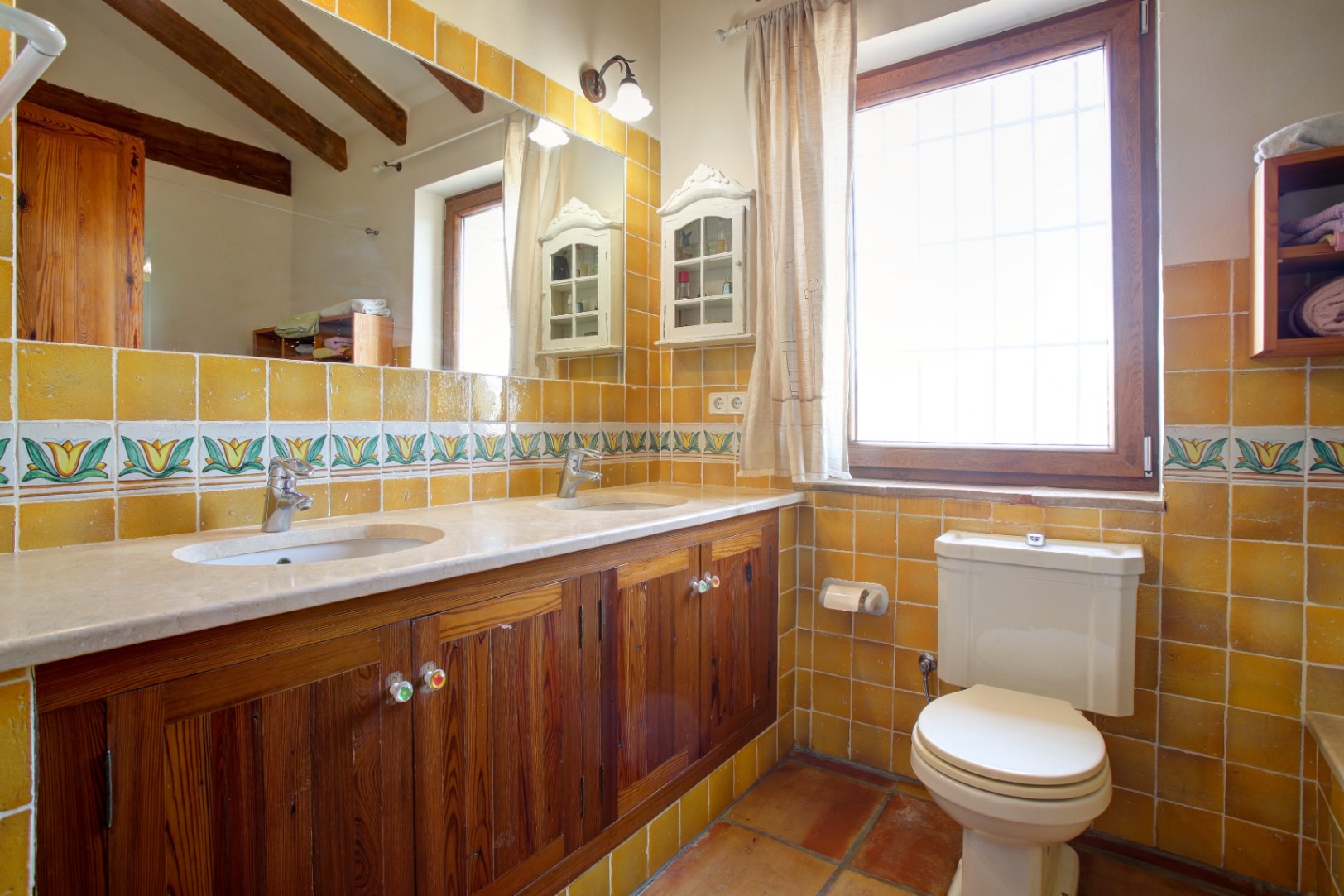 Rustic bathroom featuring a cream marble double vanity, mobila wood cabinetry, and mustard tiles. Exposed ceiling beams and terracotta flooring enhance the traditional style.